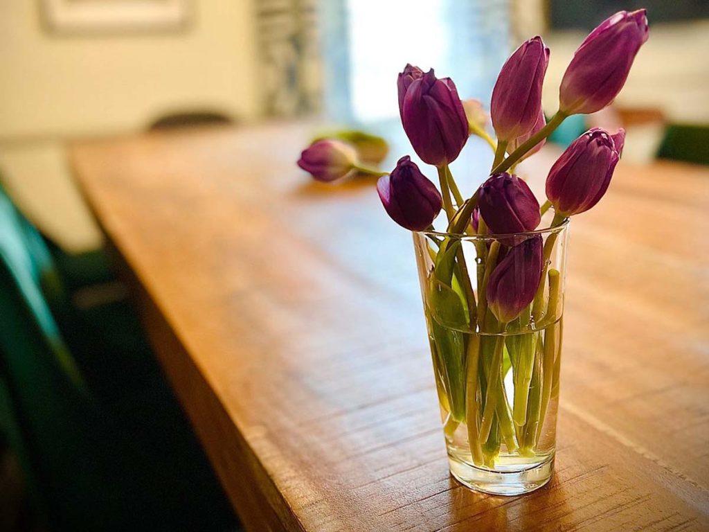 Purple tuplips in a glass vase sit on a wood table.