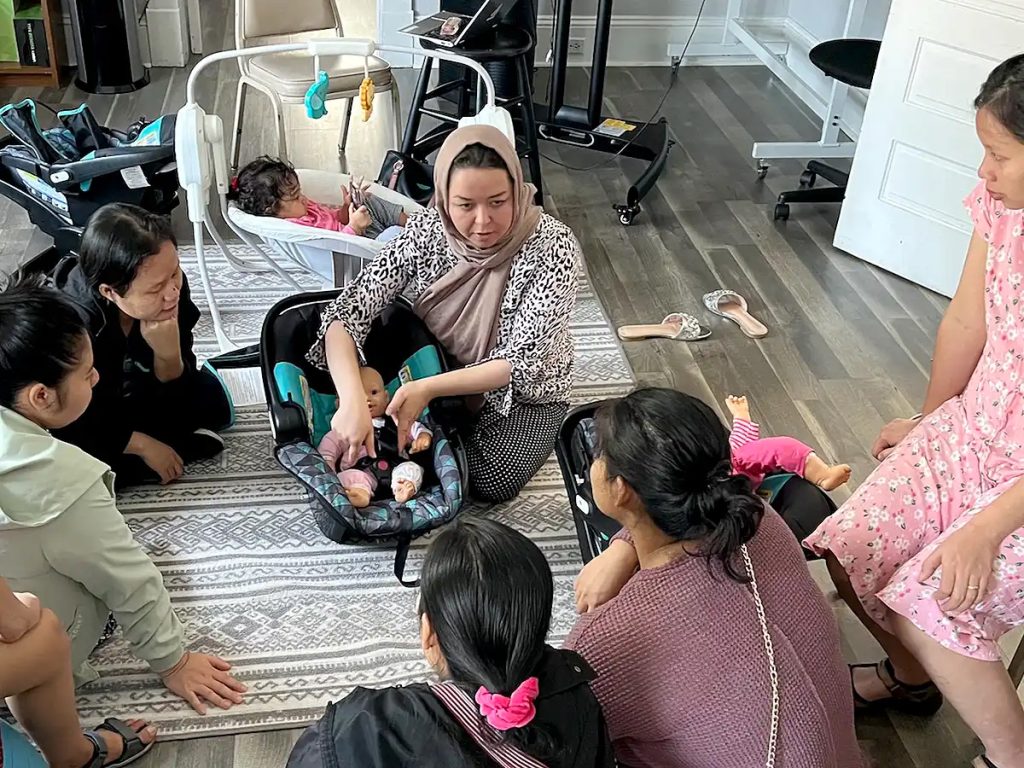 A woman demonstrates how to use a child car seat to a group of women.