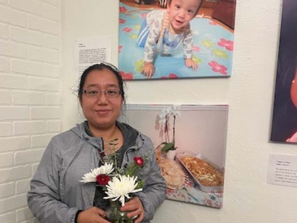 A woman holding flowers stand in front of several photographs.