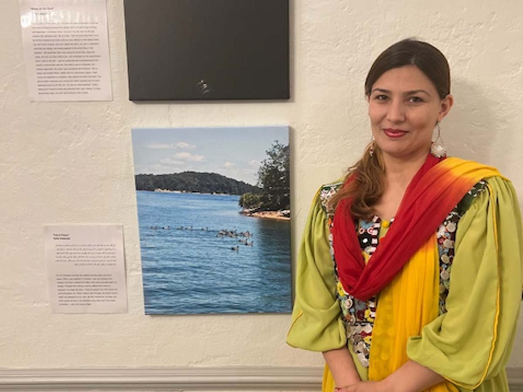 A woman stands next to a photograph hanging on a wall.