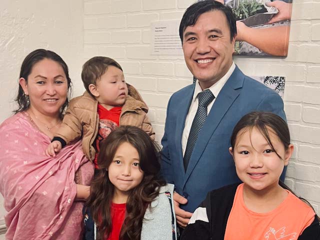 A family stand in front of a photo hanging on a wall.