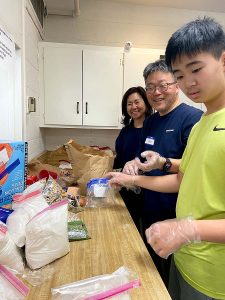 A mother, father and son stand at a kitchen counter filling storage bags with food staples.
