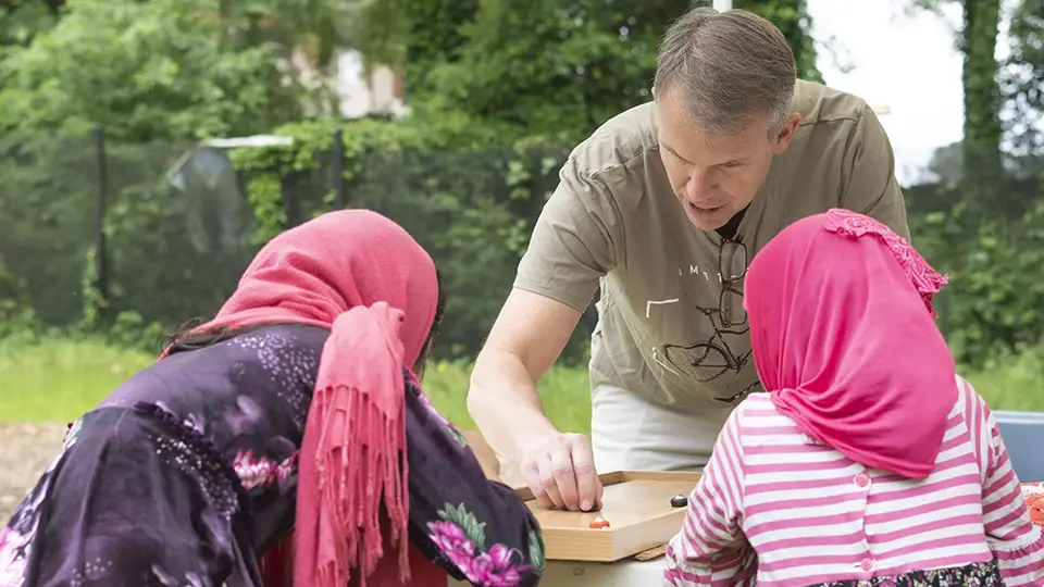 A volunteer plays a table game with two girls at Friends of Refugee's Springfest.