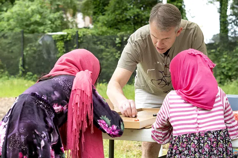 A volunteer plays a tabletop game with two young refugee girls at a Friends of Refugees event.