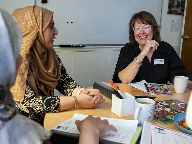 A Parwana instructor sits at a round table full of books, pens and tea, while laughing with her students.
