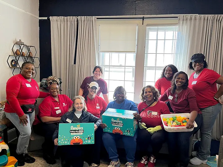 A group of Embrace Refugee Birth volunteers pose for a photo in front of windows and curtains.