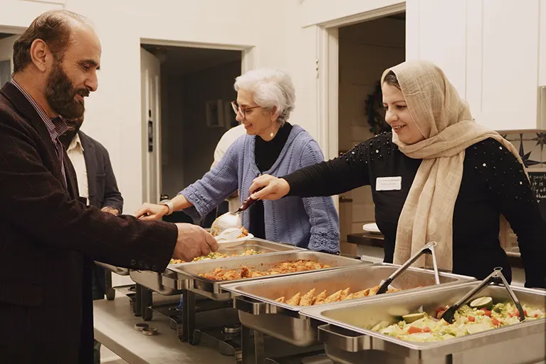 Fareshta, a Friends of Refugees client, and Helen, a board member, serve catered food at a Friends of Refugees event.