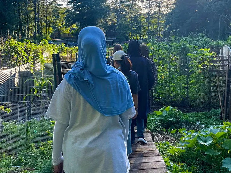 A group walk in single file into the Jolly Avenue Garden.