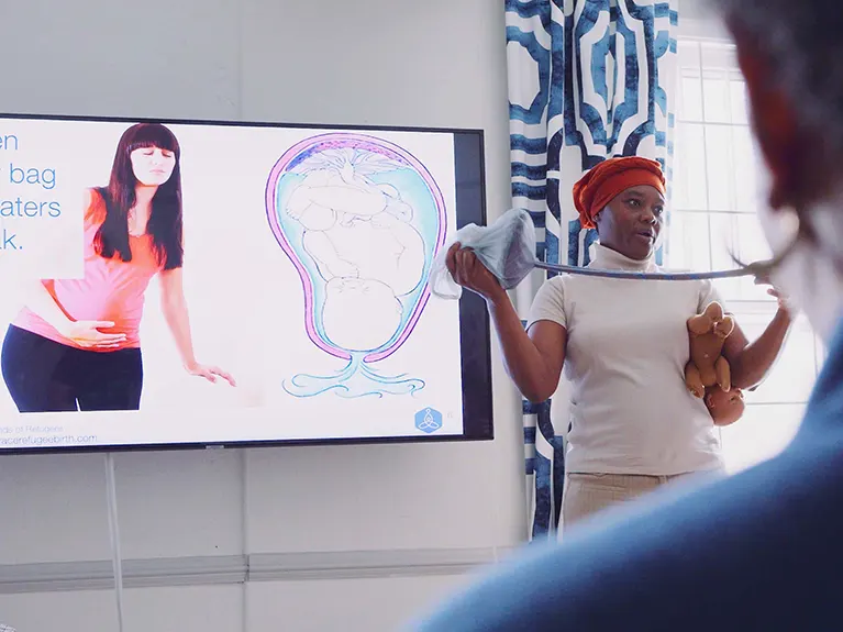 An Embrace Refugee Birth instructor holds an instructional doll while leading a Healthy Moms class.