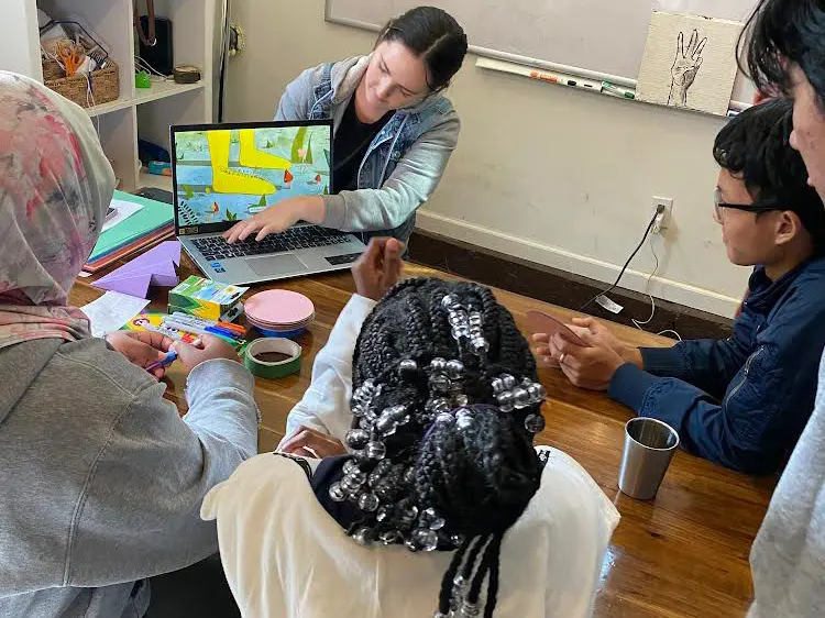 A volunteer uses a laptop to instruct a group of refugee teens during a Refugee Youth program.