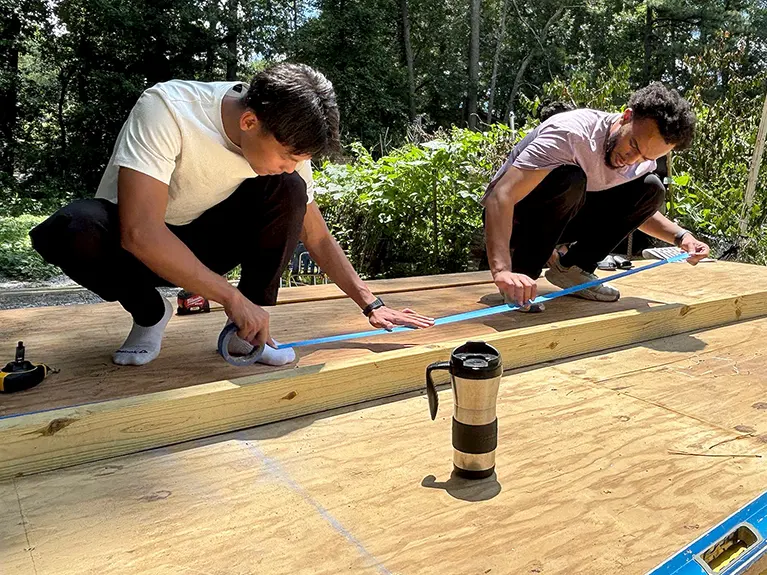 Two interns lay down a long strip of tape on a building project.