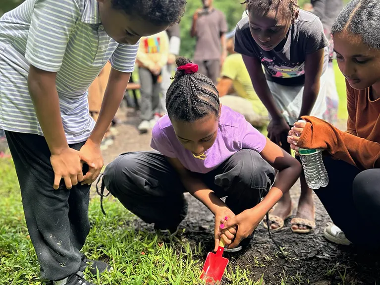 A refugee child digs in the ground while three others watch, during a Refugee Youth Afterschool Club.