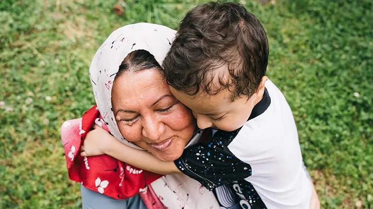 A smiling refugee mother receives a hug from her young child.