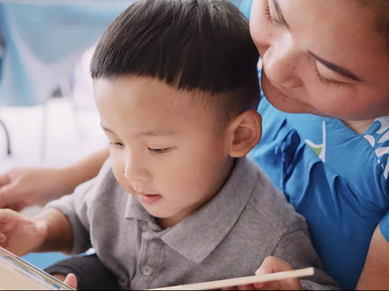 A refugee mother holds her toddler in her lap while reading a book together.