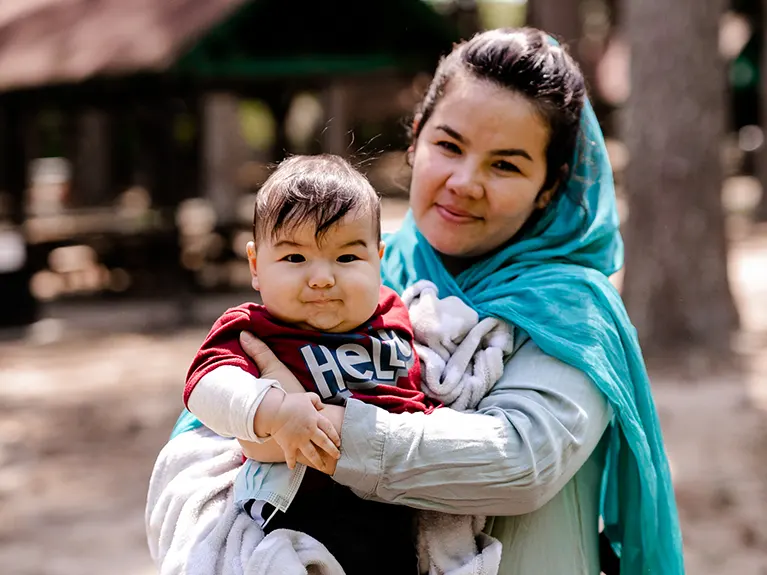 A refugee mother holds her infant while posing outside for a photo.