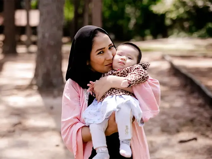 A refugee mother holds her infant while kissing her on the cheek.