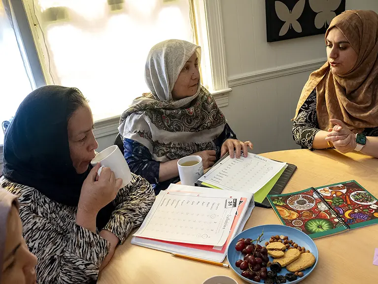 Four Parawana students drink tea and sit around a table full of notebooks and a plate of snacks.
