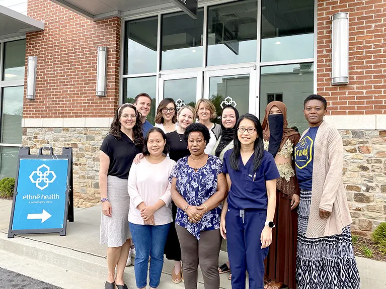 A group of leaders and staff from Friends of Refugees, Embrace Birth Support and Ethne Health stand in front of the entrance to Ethne Health.