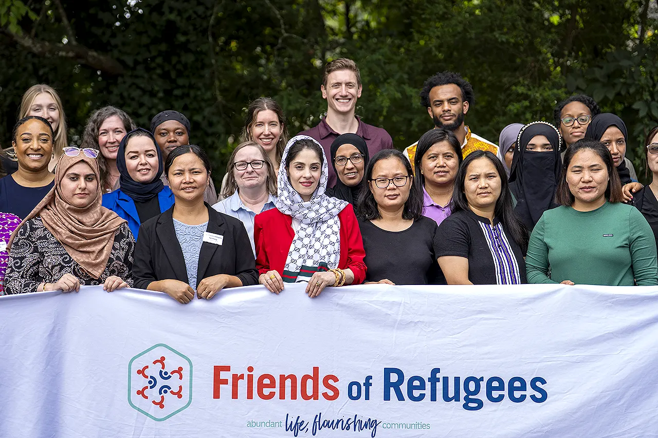 A large group of Friends of Refugees staff stand outside holding a banner with the organization's logo.