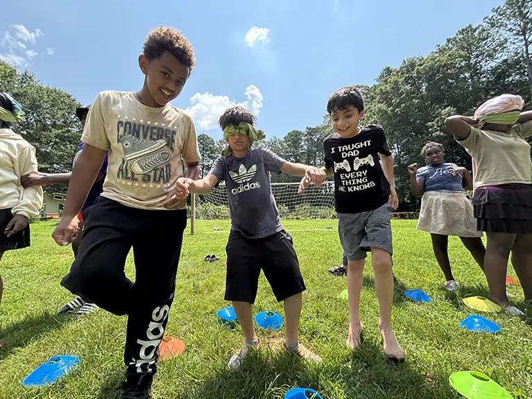Two boys lead a blindfolded boy by his hands at a Summer Pathfinders event.