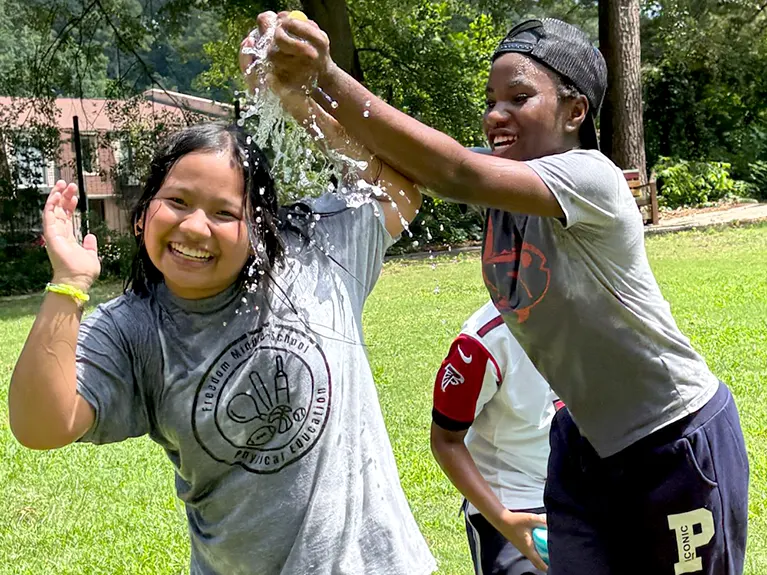 Two girls participate in a water ballon fight at a Friends of Refugees youth program event.
