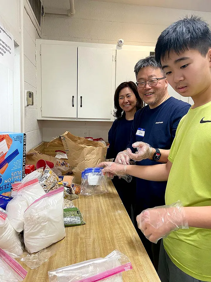 A mother, father and son prepare food kits at a kitchen counter.