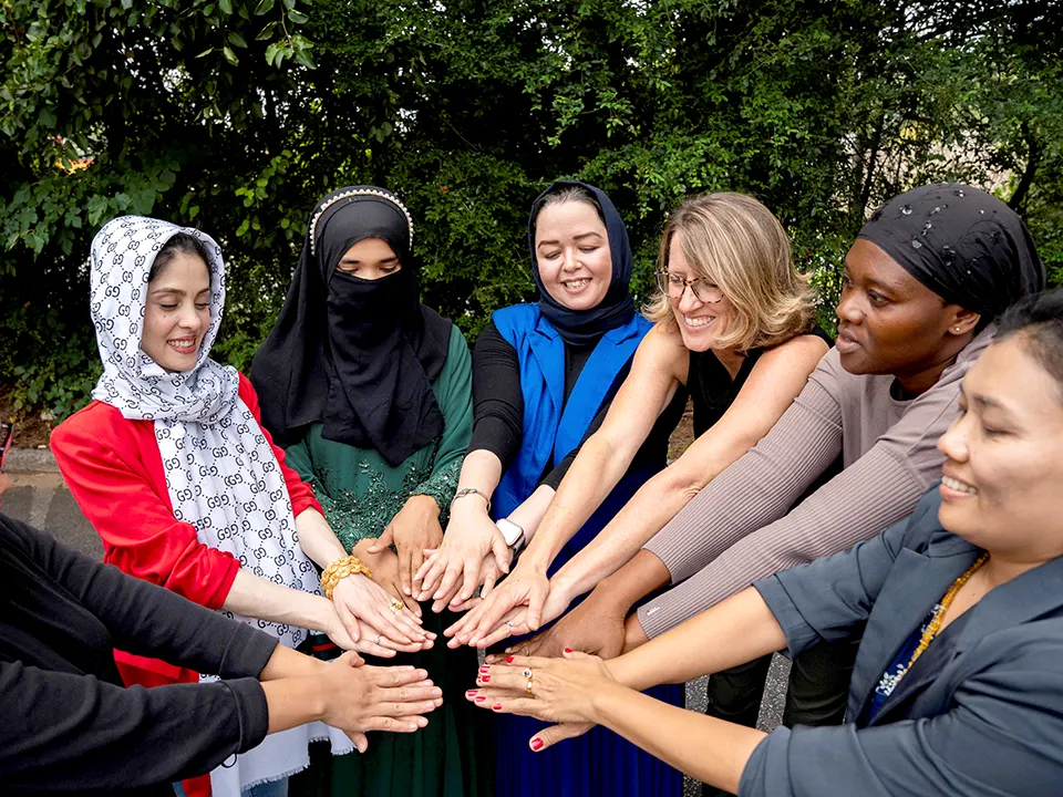 A group of Friends of Refugees staff members stand in a circle with their hands touching at the center.