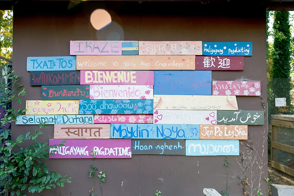 A wooden wall with wood slat signs reading, "Welcome" in various languages.