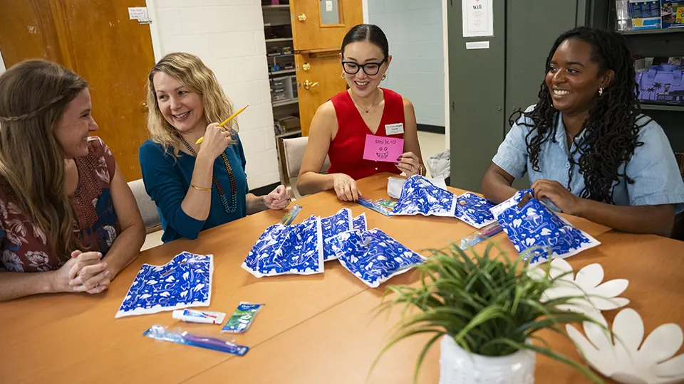 Four smiling women sit around a table at the Friends of Refugee's office.