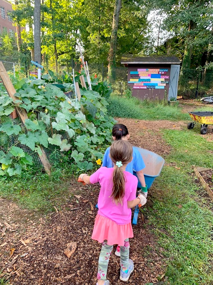 Two girls push a wheelbarrow through the Jolly Avenue Garden in Clarkston, GA.